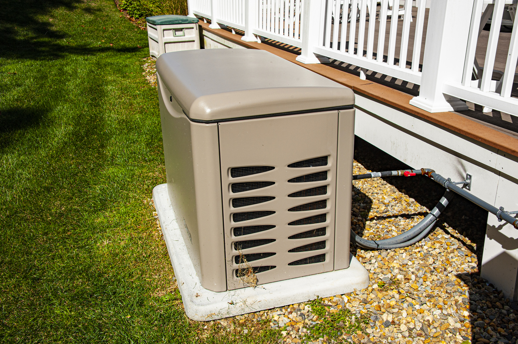 Tan generator in the yard by a back deck with some weeds in the unit