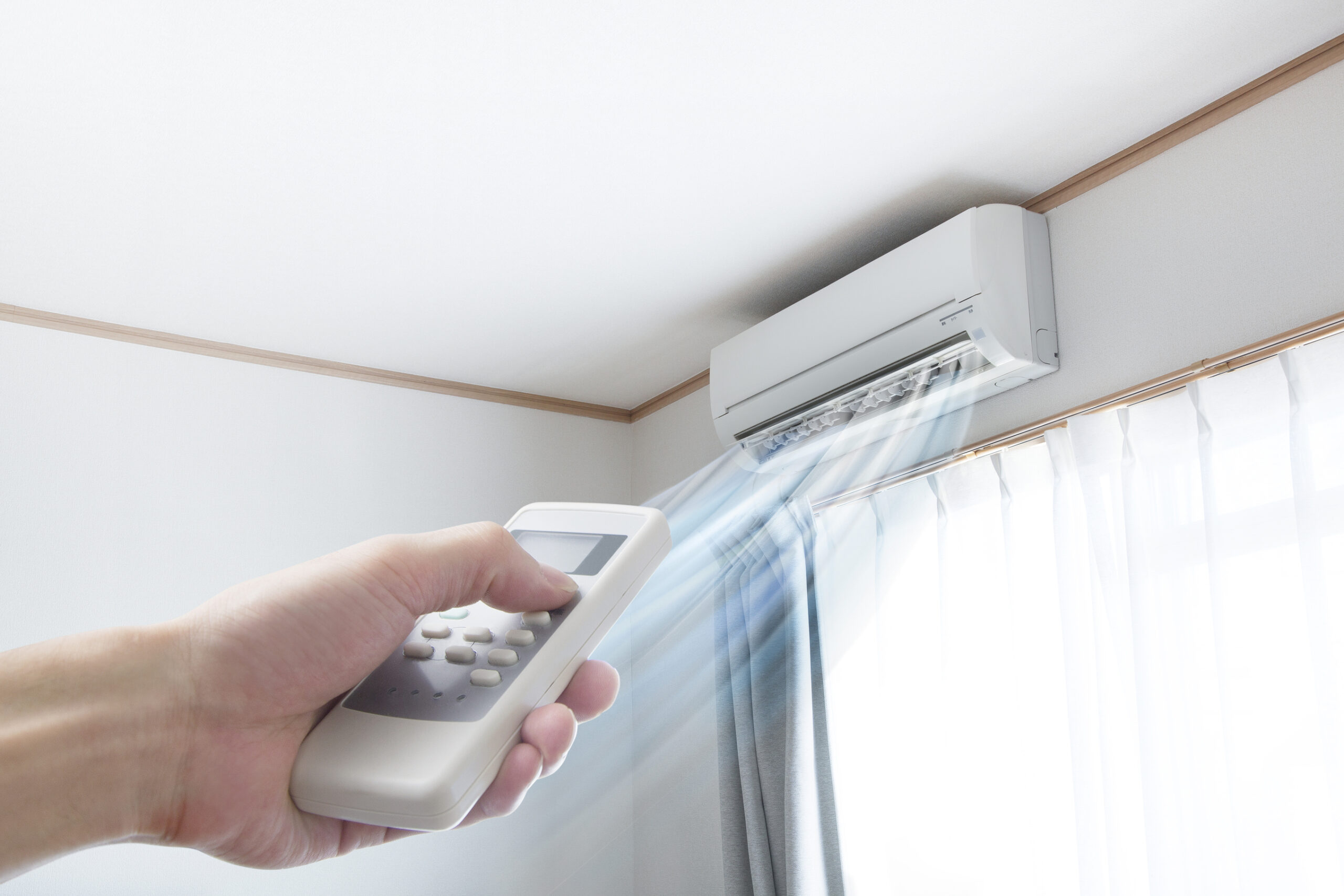 A woman’s hand pointing a remote at a ductless mini-split unit