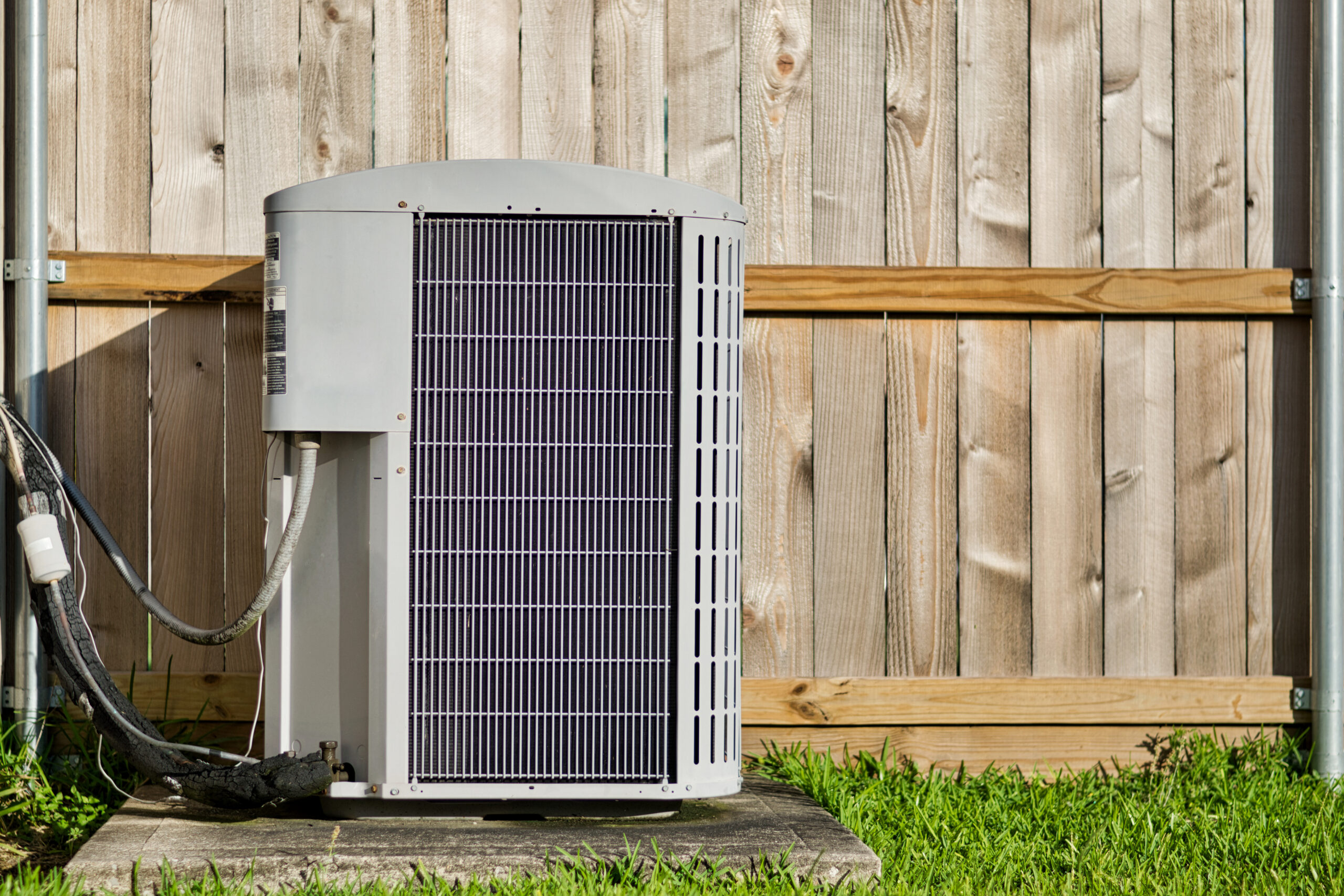 AC unit in a backyard against a wooden fence