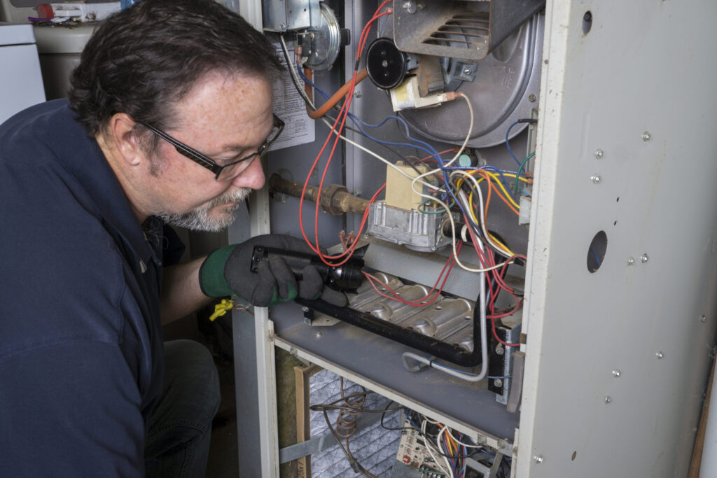 Technician looking over a gas furnace with a flashlight before cleaning it