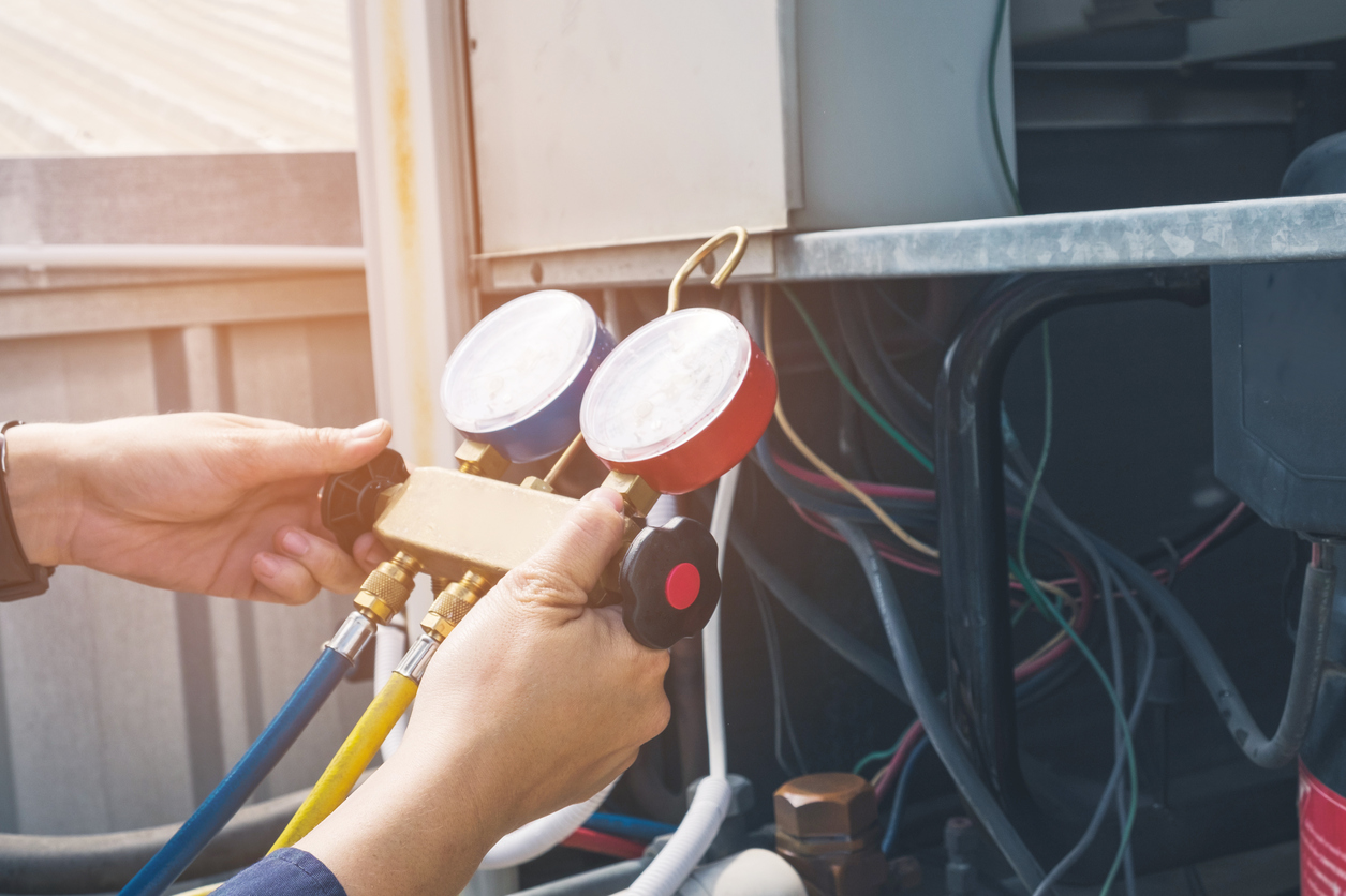 Commercial HVAC technician using a pressure gauge on an AC unit during a maintenance service