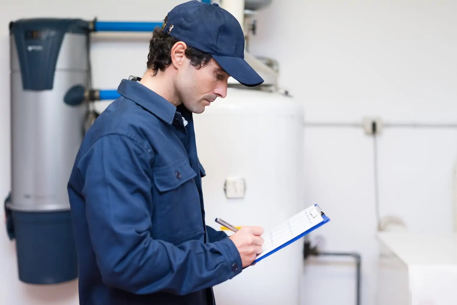 A plumber with a clipboard checking a new water heater installed in a Michigan home